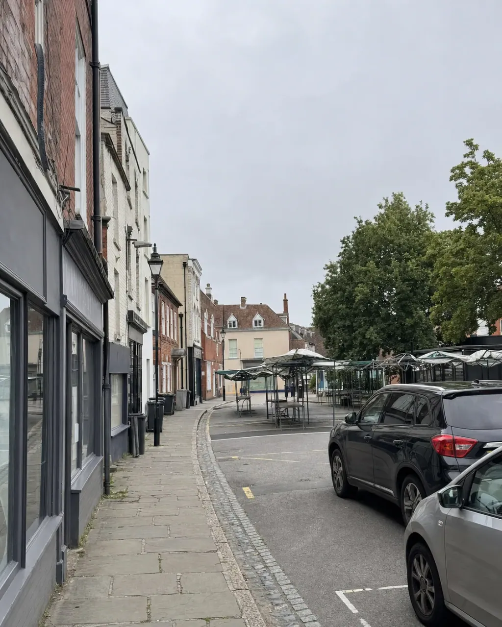 A Newport Pagnell street of brick and painted render buildings of mixed ages, with a small open market area and covered stalls at the roadside