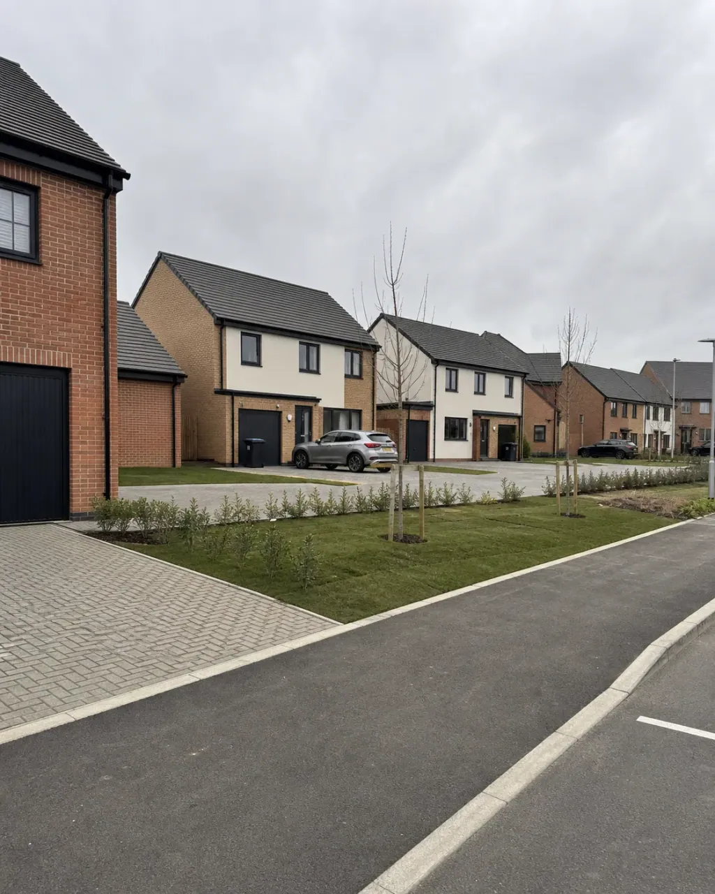 A very new Whitehouse development of brick and pale render houses with crisp block paving, saplings still staked and wide open sky above