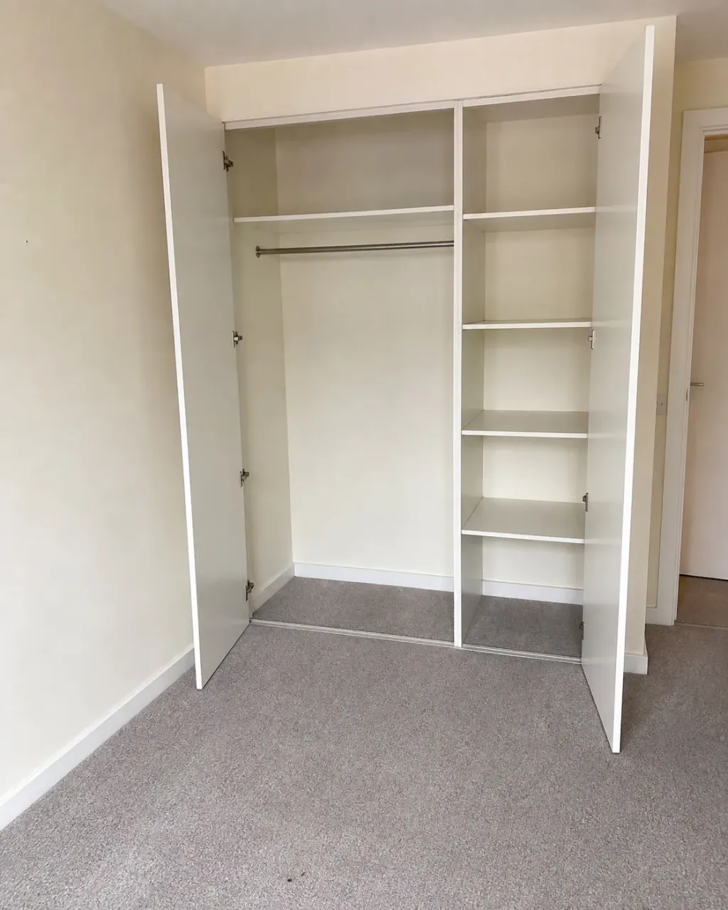 A built-in wardrobe standing open in an empty Milton Keynes bedroom, its shelves and hanging rail completely bare and wiped clean